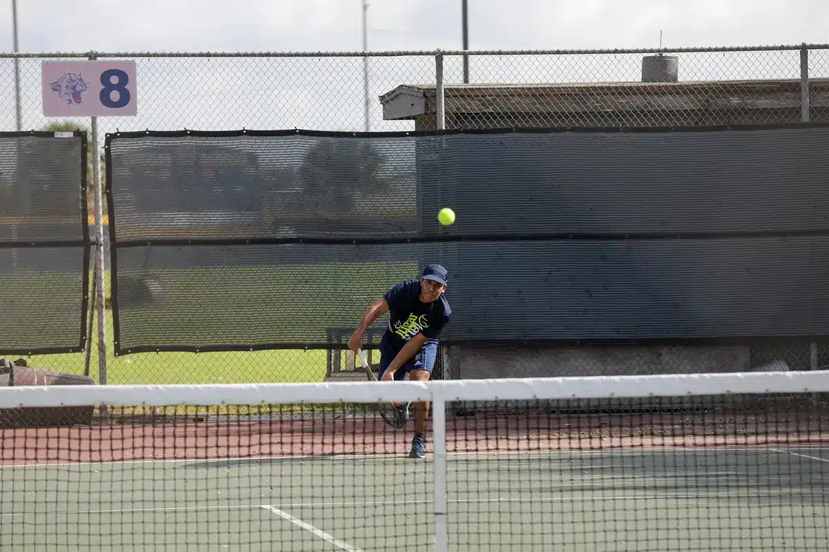 A close-up of an unbranded tennis racket and ball resting on a hardcourt, faint court lines visible, no players or logos