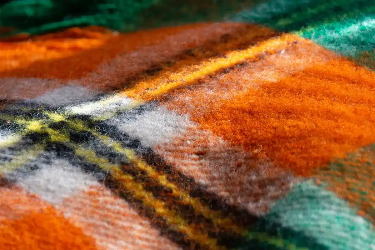 Close-up of fabric texture with hexagonal pattern and bright yellow pigment catching sunlight, no brand marks, on a generic studio table beside a sewing machine.