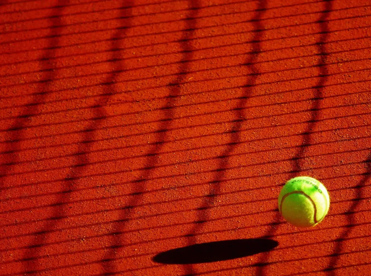 Empty central court at dusk with a single tennis ball on the baseline, subtle stadium lights coming on