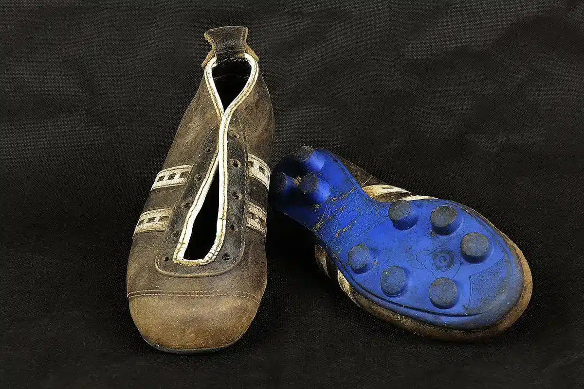 Anonymous close-up of a striker's unbranded boots striking a ball on wet grass, droplets flying from impact