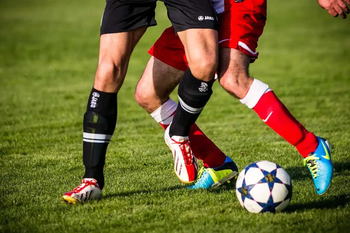 A close-up of an empty football boot on wet grass beside a white pitch line, suggesting a match about to start