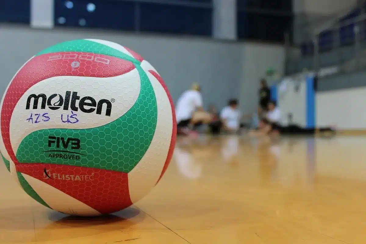 Empty indoor arena with an unbranded volleyball net and a single ball on the polished court, low camera angle, empty stands in the background